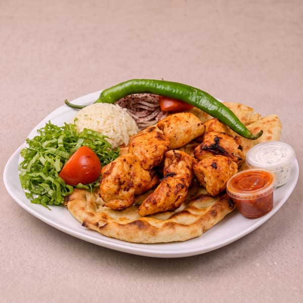 Grilled chicken skewers with rice, salad, flatbread, green pepper, and two sauces on a white plate.
