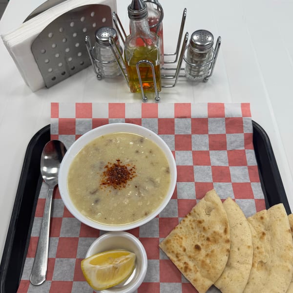 Creamy soup with red pepper flakes, lemon, and flatbread on a checkered tray with condiments.