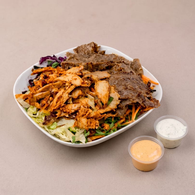 A white bowl filled with mixed salad, chicken, and beef, with two sauce cups beside it.