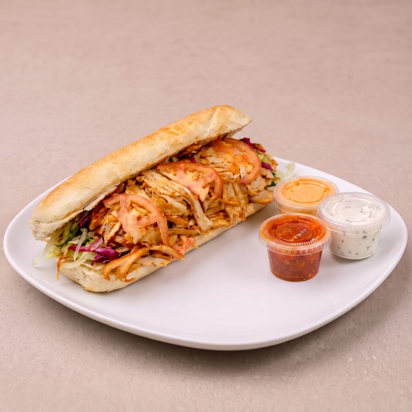 Chicken doner kebab in a baguette with salad and three sauce pots on a white plate.