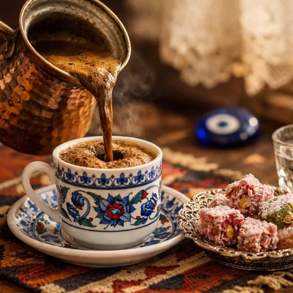 Traditional Turkish coffee poured from a cezve into a cup, served with Turkish delight and water.