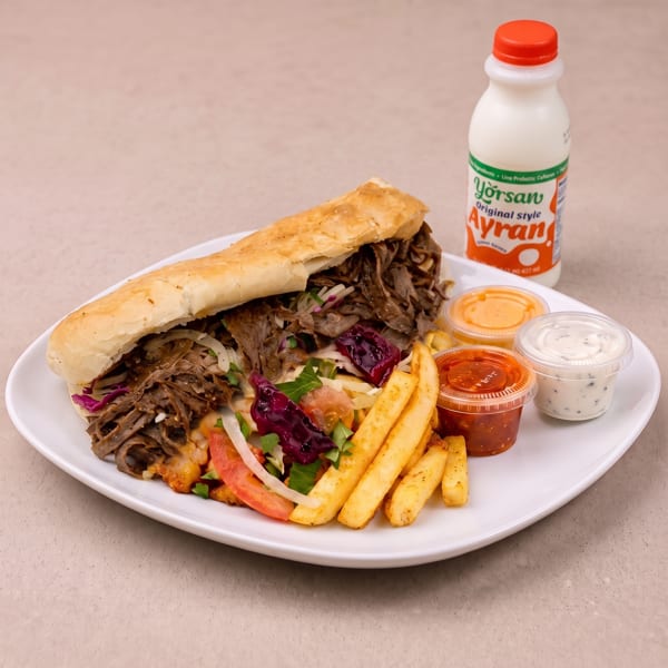 Doner kebab sandwich with fries, salad, three dipping sauces, and a bottle of Ayran.