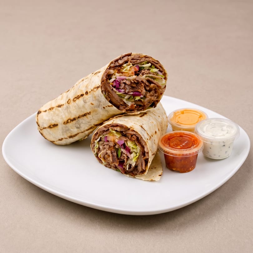 Two doner kebab wraps, filled with meat and vegetables, served with three dipping sauces on a white plate.