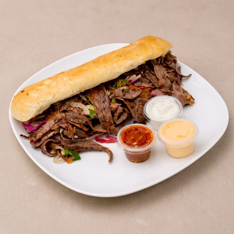 A large beef shawarma sandwich on a white plate, served with three dipping sauces.